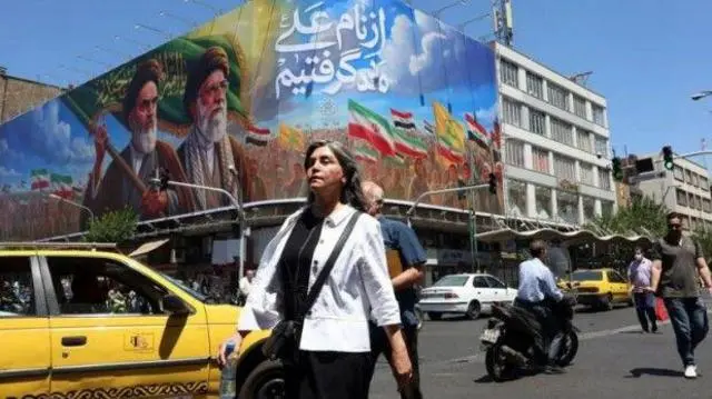 لوحة إعلانات كبيرة تحمل صورة المرشد الإيراني الراحل علي خامنئي وإلى جانبه الخوميني - في ميدان بإيران حيث يمرّ عدد من الأشخاص